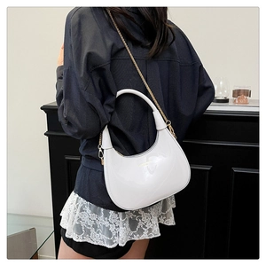 Detail of white glossy leather crescent bag with gold chain strap shown on a model