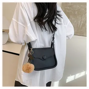 Minimalist black leather crossbody bag with rounded flap and plush khaki pom-pom charm