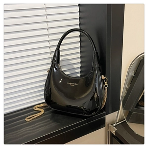 Detail of high-gloss black crescent bag with gold chain and logo text on the side