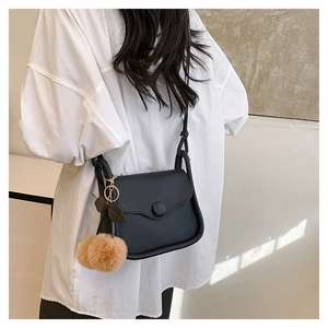Detail of black crossbody bag with round buckle and fluffy brown ball ornament on model