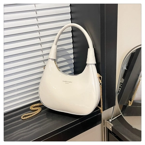 Detail of white patent leather crescent bag with gold chain and metal hardware accents