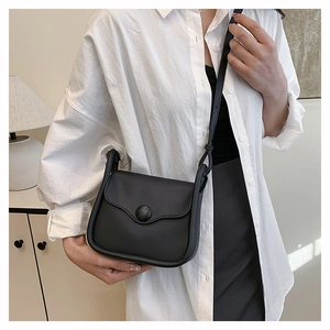 Detail shot of a black leather crossbody bag on a model in a warm indoor setting