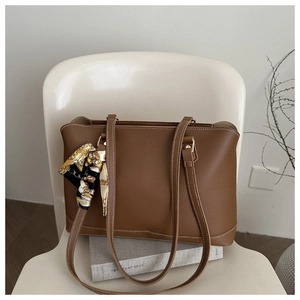 Detail of a brown tote bag featuring white contrast stitching and a patterned silk scarf