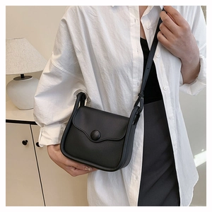 Detail of a black crossbody bag with matte leather and round button closure on a model