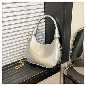 Detail of silver metallic hobo bag featuring CAHPES & HEKG logo and gold chain strap