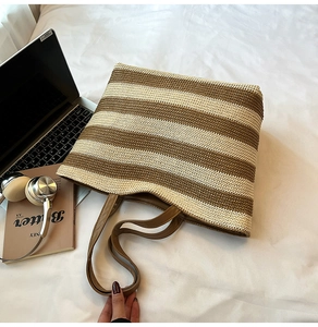 Détail d'un grand cabas tissé avec rayures contrastées et longues anses posé sur un lit