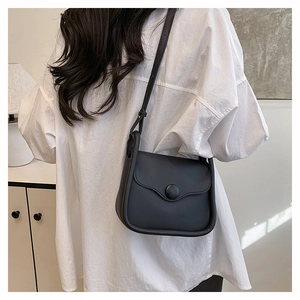 Detail of minimalist black leather crossbody bag with iconic round buckle on circular flap