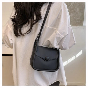 Detail of minimalist black crossbody bag with wave edge flap and large covered button
