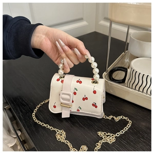 Detail of white leather mini bag with cherry print and decorative pearl handle