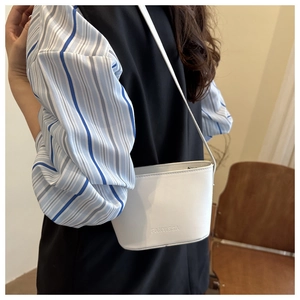 Close-up of a white leather bucket bag with FANYISSA embossed logo on striped shirt