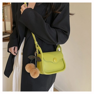 Detail of avocado green saddle bag with magnetic closure and plush cherry charm on model