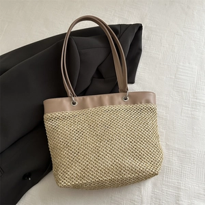 Fashionable straw tote bag with brown leather straps displayed on a grey blazer