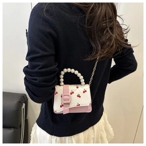 Mini pink crossbody bag with cherry print and pearl handle shown on a model