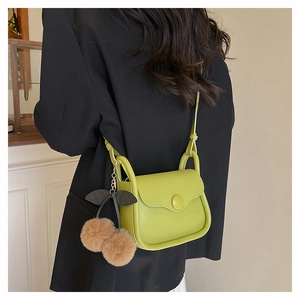 Detail of lime green crossbody bag with cherry charm worn on a black blazer suit
