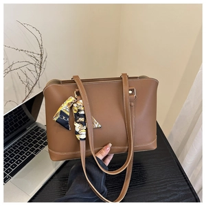 Detail of a brown tote bag with contrast stitching and decorative silk scarf on handle