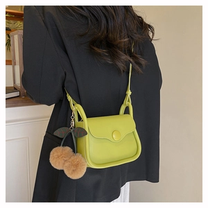 Detail of avocado green crossbody bag with cherry pom-pom charm on black blazer