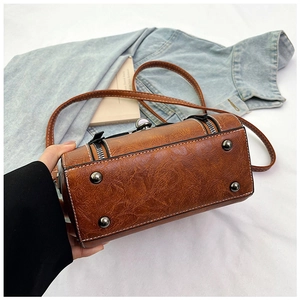 Detail of vintage brown cylinder crossbody bag with protective metal studs and smooth texture