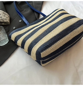 Détail du sac cabas en paille à rayures marines sur fond de literie blanche