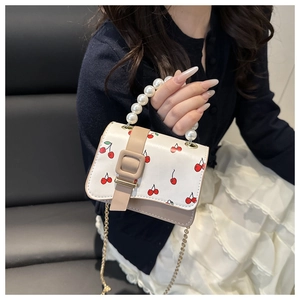 Detail of white leather mini bag with cherry prints, pearl handle, and chain strap
