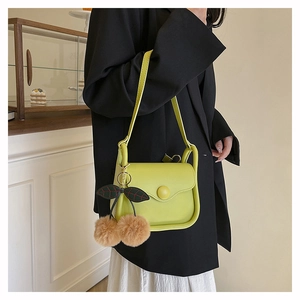 Detail view of avocado green crossbody bag with cute cherry plush charm on suit