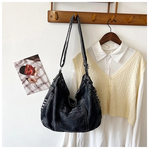 Detail of washed black denim hobo bag with frayed edges hanging on a wooden hook