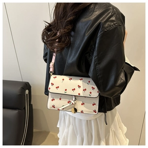 Détail du sac bandoulière blanc à motif cerise avec sangle rose et breloque dorée