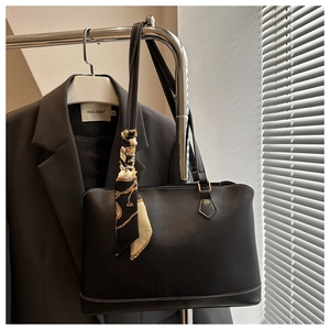 Close-up of black leather tote bag with contrast stitching and decorative silk scarf