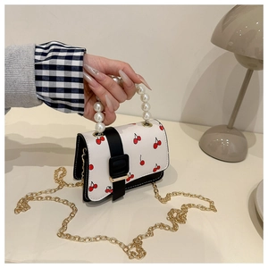 Close-up of a white mini bag with cherry prints, pearl handle, and gold metal chain strap