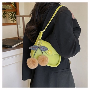 Detail of neon green PU leather shoulder bag featuring plush cherry charms on black blazer