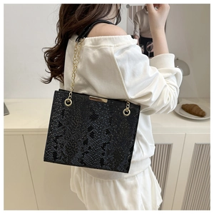 Detail of black snake pattern crossbody bag with gold chain strap and metal buckle