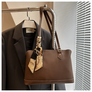 Close-up of brown leather tote bag featuring elegant silk scarf handle and golden hardware