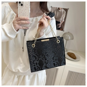 Detail of black snakeskin texture tote bag with gold chain strap and metal bar trim