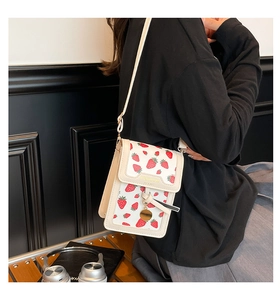 Close-up of a white leather crossbody phone bag with strawberry print and gold hardware