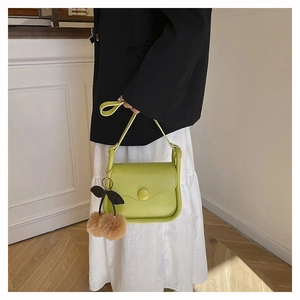 Detail view of avocado green crossbody bag with cherry plush charm on white wall backdrop