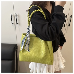 Détail d'un sac cabas tressé vert herbe avec un foulard décoratif en soie sur l'anse