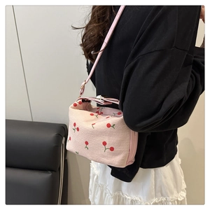 Dettaglio ravvicinato della borsa intrecciata rosa con motivo a ciliegia e chiusura a fiocco