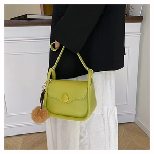 Close-up of lime green PU leather shoulder bag with circular buckle and brown pom-pom charm