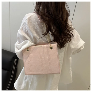Pink snake-embossed leather chain bag shown on model with a white shirt and golden strap