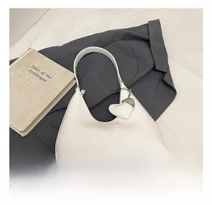 Close-up of white patent leather hobo bag with heart pendant and bottom metal studs