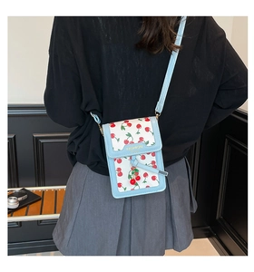 Detail of light blue square crossbody bag with cherry prints and a fashion gold logo