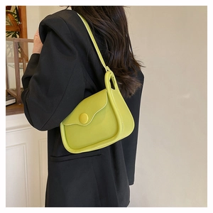 Detailed view of avocado green leather shoulder bag with circular button on black blazer
