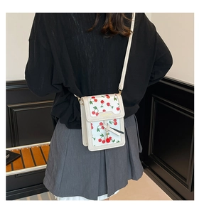 Detail of cream-white cherry print crossbody bag with gold fashion plaque and red pendant