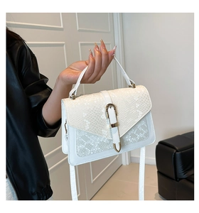 Detail of white snakeskin texture handbag with gold buckle and crossbody strap on black leather