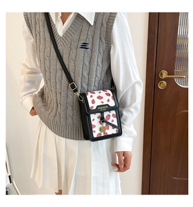 Detail of sweet strawberry print crossbody bag with fashion logo and slim black strap