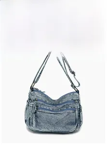 Detail of light blue washed denim crossbody bag with multiple zipper pockets and brass hardware