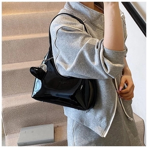 Detail of glossy black patent leather underarm bag with heart charm and brand lettering