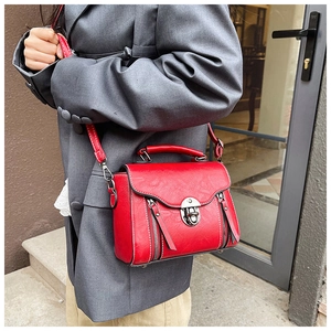 Vintage red crossbody bag with metal clasp and side zippers held by a woman in a grey suit