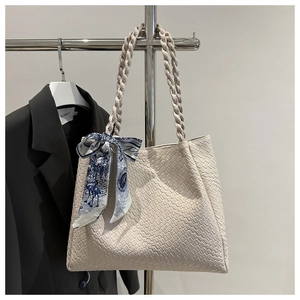 Détail du sac cabas tressé crème avec poignées tressées et foulard en soie décoratif
