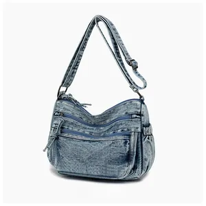 Macro view of blue denim crossbody bag featuring multi-layer zip pockets and aged hardware