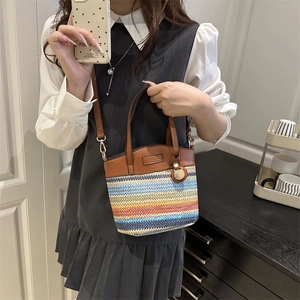 Sac seau en paille rayée arc-en-ciel avec anses en cuir porté par un mannequin en intérieur